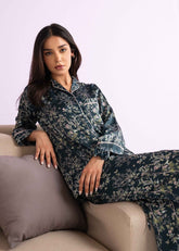 A woman sitting on a couch, wearing a floral print PJ set with a button-down shirt and matching pants.